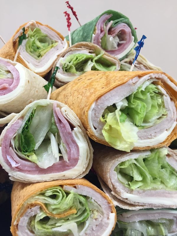 A cluster of colorful tortilla wraps filled with deli meat, cheese, and lettuce, secured with small decorative toothpicks.