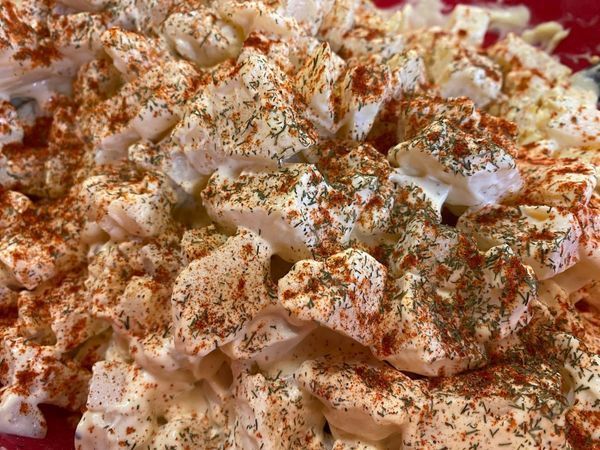 A close-up view of potato salad in a red bowl, topped with a generous sprinkle of paprika and dried herbs.