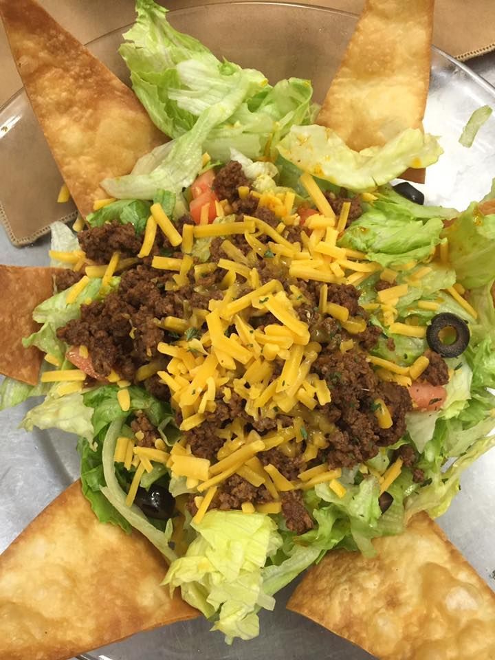A taco salad topped with ground beef, shredded cheddar cheese, and black olives, served with crisp tortilla chips.