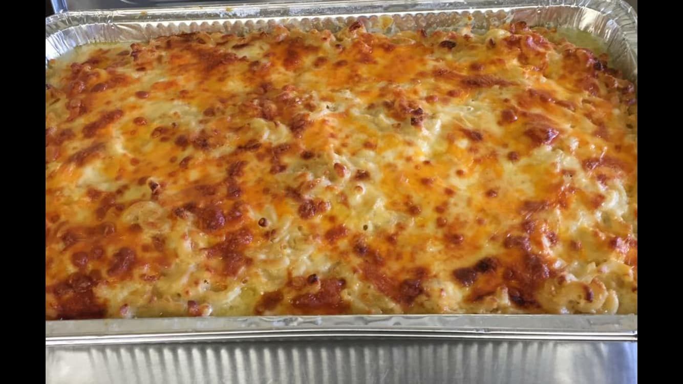A rectangular aluminum tray filled with baked macaroni and cheese topped with golden-brown, melted cheese.