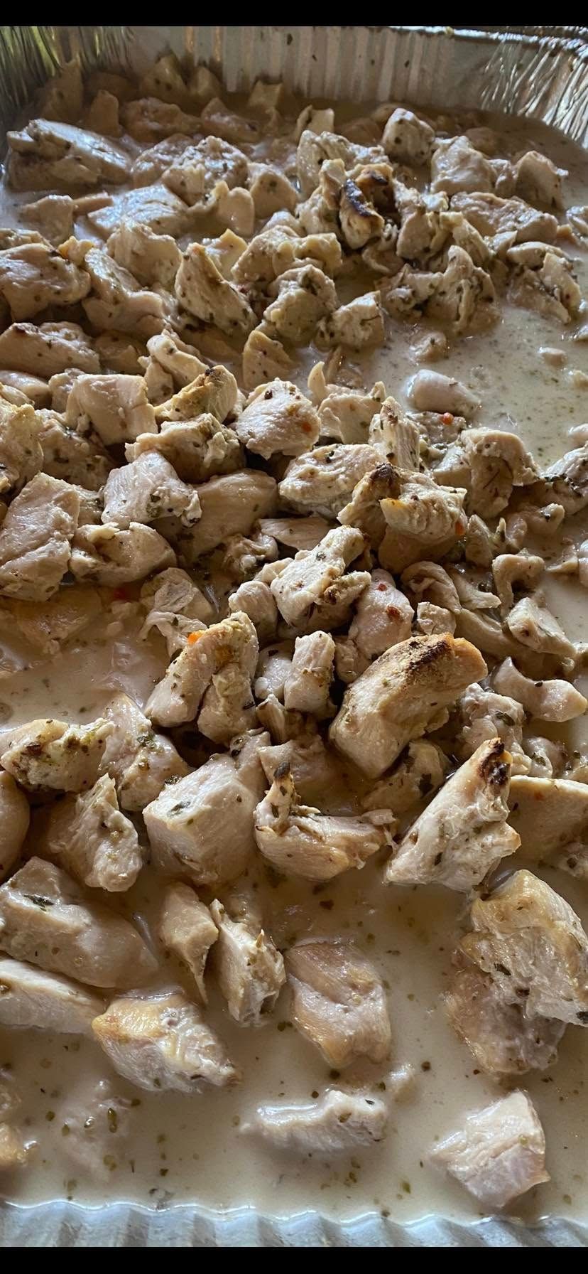 A metal pan filled with diced, seasoned cooked chicken pieces in a creamy white sauce.