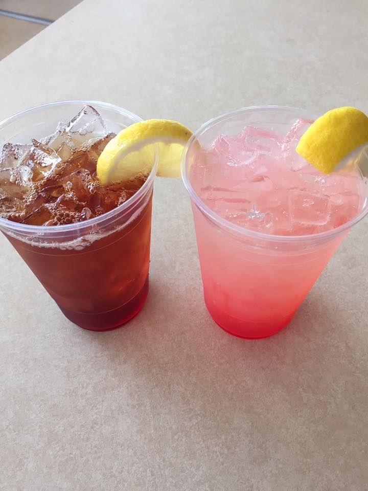 Two clear plastic cups filled with ice, one containing iced tea and the other pink lemonade, each garnished with a lemon.