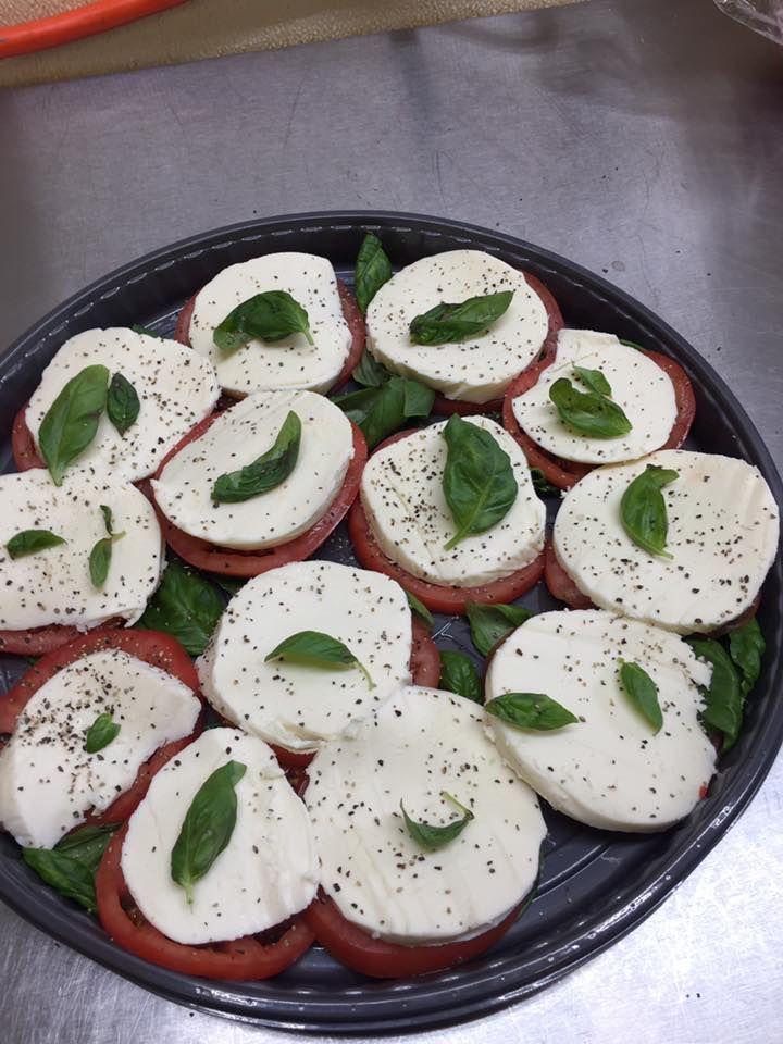 A platter of Caprese salad with slices of fresh mozzarella, tomatoes, and basil leaves seasoned with black pepper.