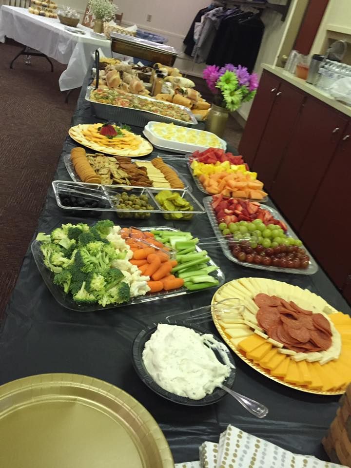 A long buffet table spread with various platters of food, including fresh vegetables, fruit, cheese, crackers, and dips.
