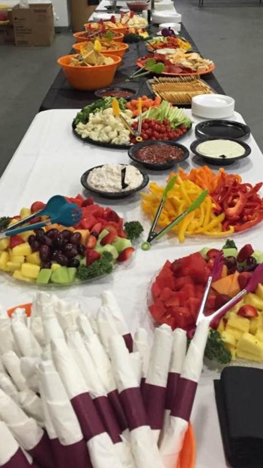 A long buffet table spread with various platters of fresh fruit, vegetables, dips, and snacks, with napkins in the front.