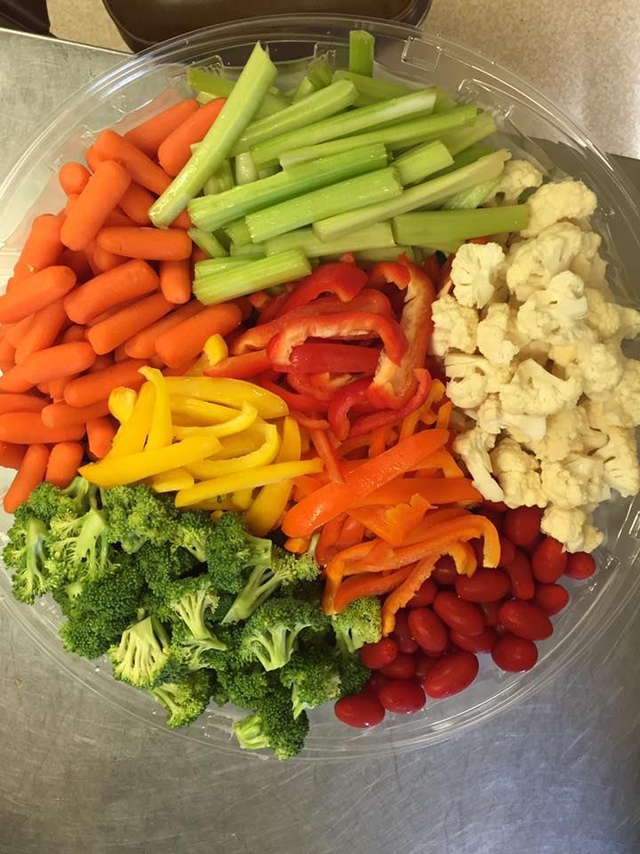 A plastic platter filled with assorted raw vegetables, including carrots, celery, peppers, cauliflower, broccoli, and beans.