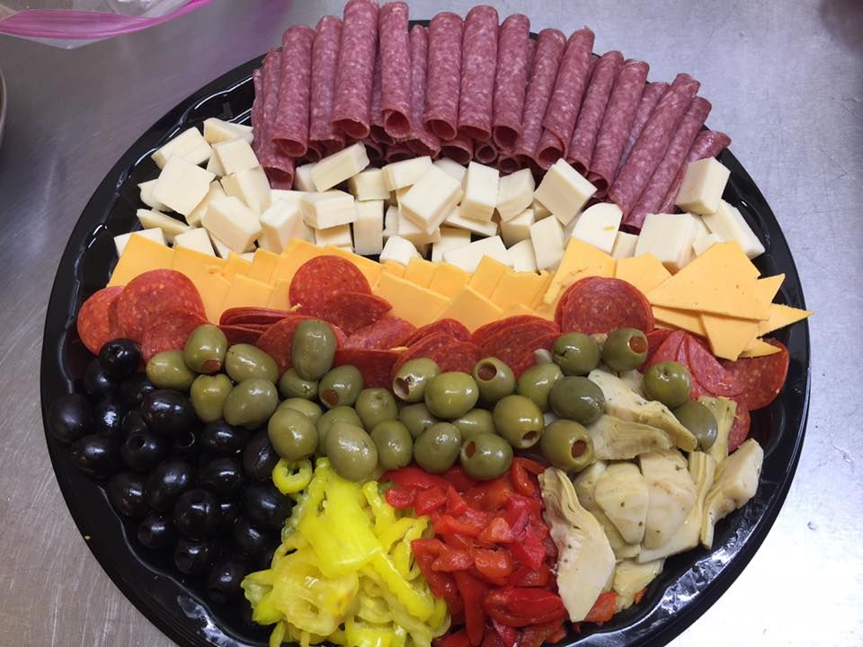 A party platter with arranged rows of salami, cubed cheese, sliced cheddar, pepperoni, olives, peppers, and artichokes.
