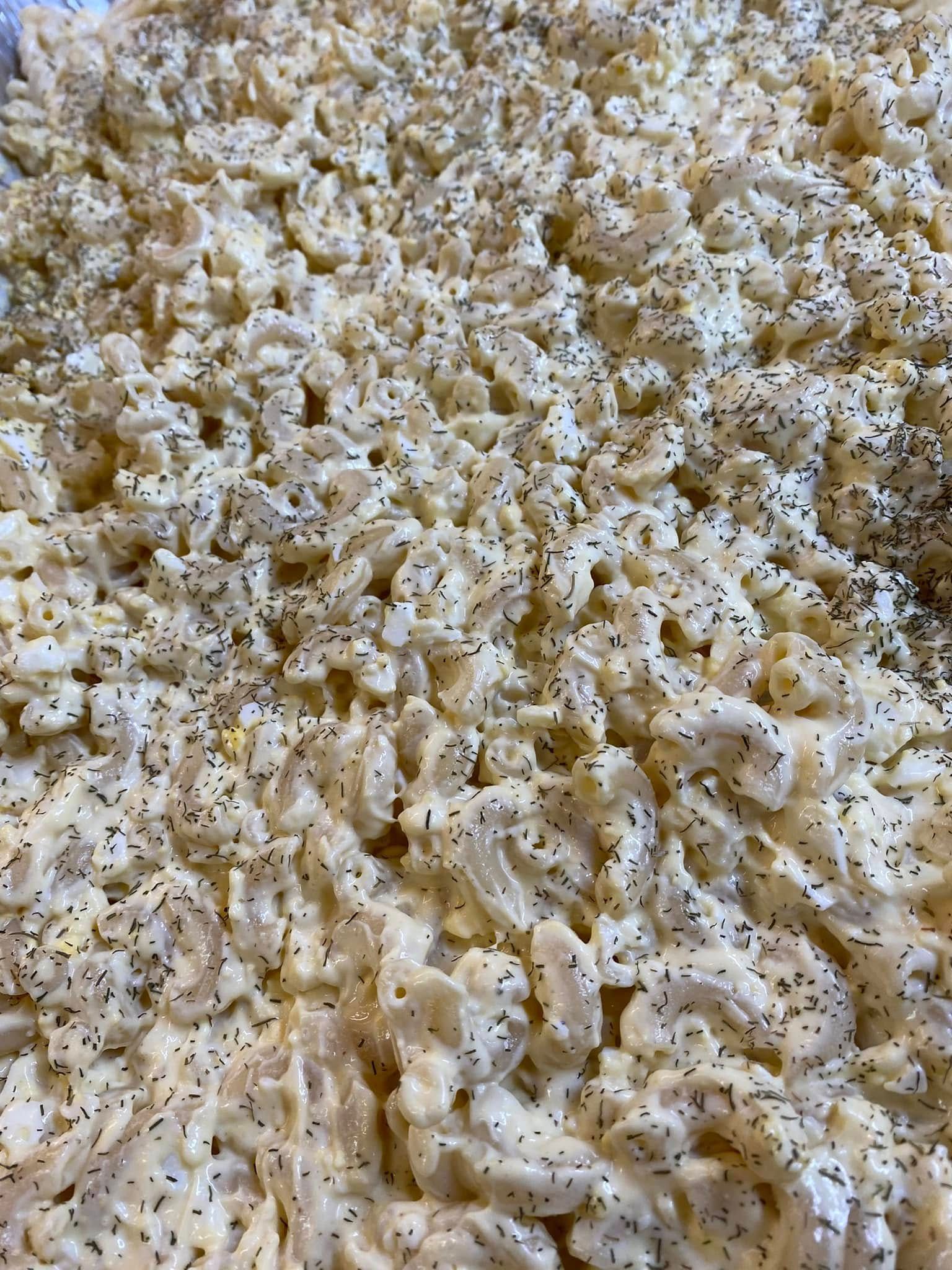 A close-up of a large serving of macaroni salad coated in a creamy dressing and generously topped with black pepper.