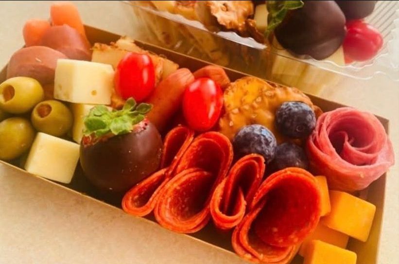 A snack box filled with cheese cubes, olives, pepperoni, cherry tomatoes, blueberries, and a chocolate-covered strawberry.