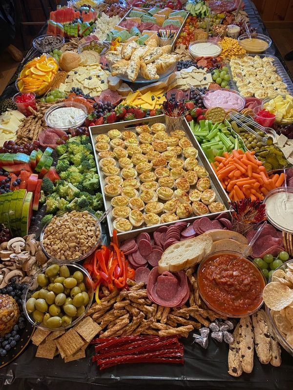 A large, rectangular table filled with an extensive variety of finger foods, charcuterie, fruits, vegetables, and dips.