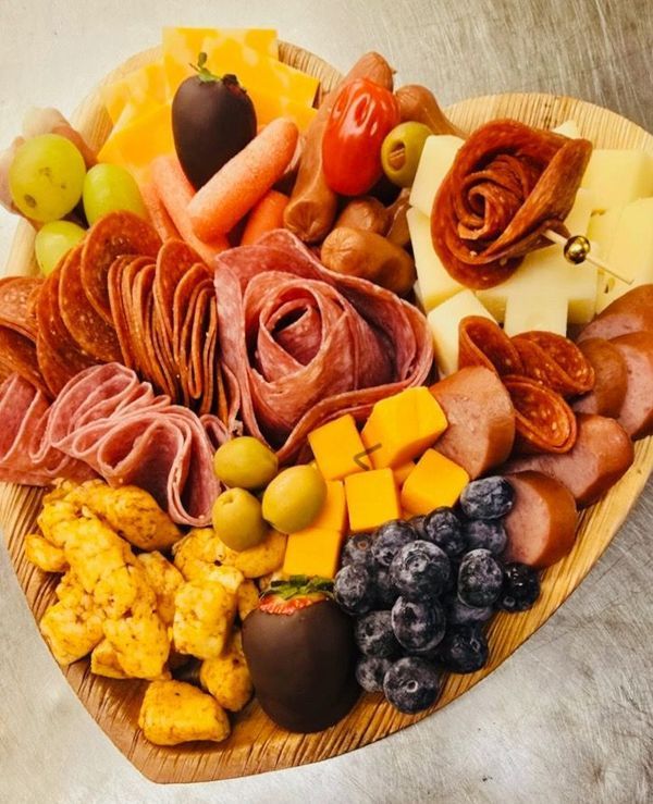 A charcuterie board with salami roses, assorted cheeses, olives, blueberries, carrots, and chocolate-dipped fruit.