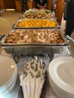 A buffet line with trays of chicken, mac and cheese, and potatoes, with stacks of white plates and silverware in front.