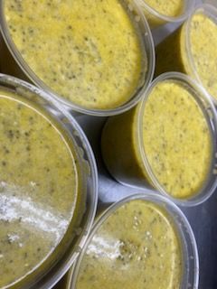 Several round, clear plastic containers filled with a thick, yellow, herb-flecked soup or sauce, arranged together.