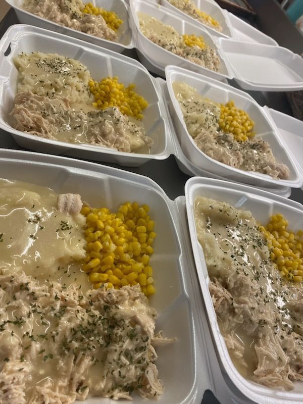 Several white partitioned takeout containers filled with shredded chicken, gravy, mashed potatoes, and yellow corn.