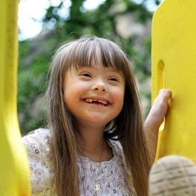Smiling child with long hair outdoors, holding a bright yellow playground structure
