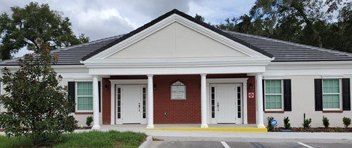 Single-story white building with red brick center, green shutters, and a covered front entrance
