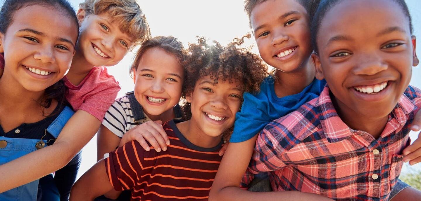 A group of children are together looking at the camera. The sky is behind them.