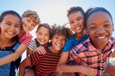 Five smiling children sitting closely together outdoors in bright sunlight
