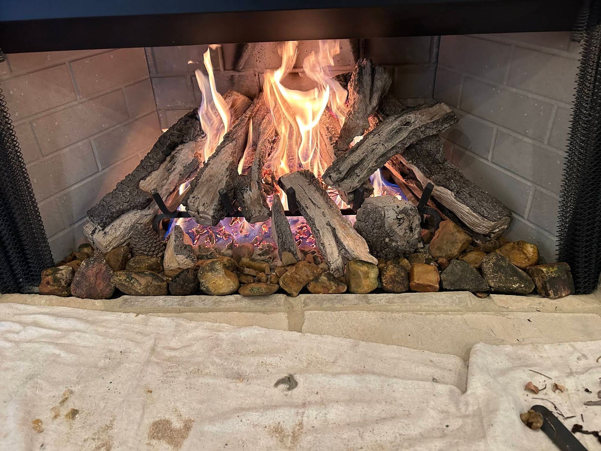 Lit fireplace with stacked logs, bright flames, and stones on the hearth.