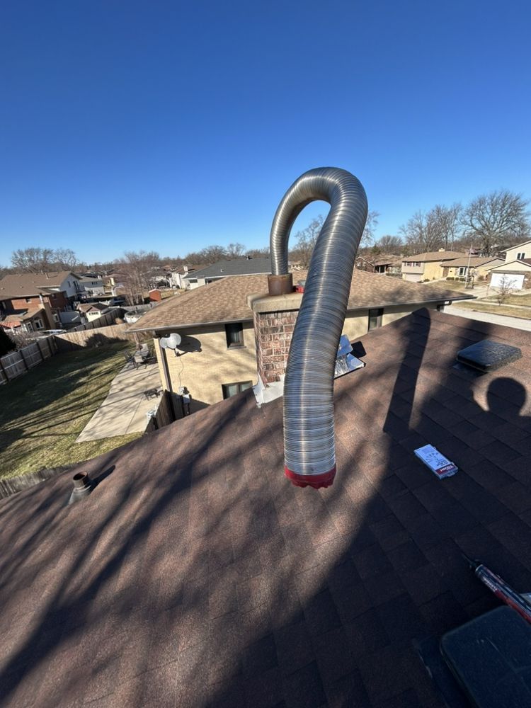 Flexible silver roof vent pipe on a shingled rooftop under a blue sky