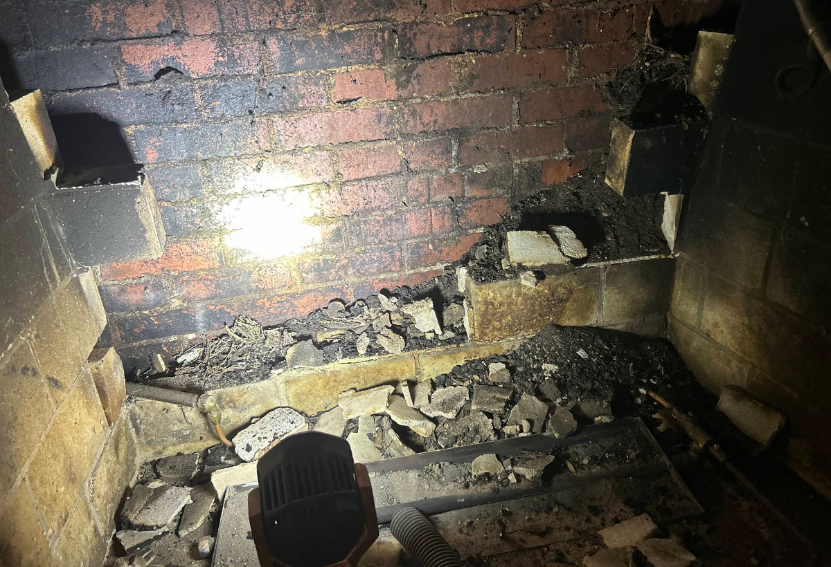 Fire-damaged brick wall and debris inside a dark fireplace or fireplace chamber