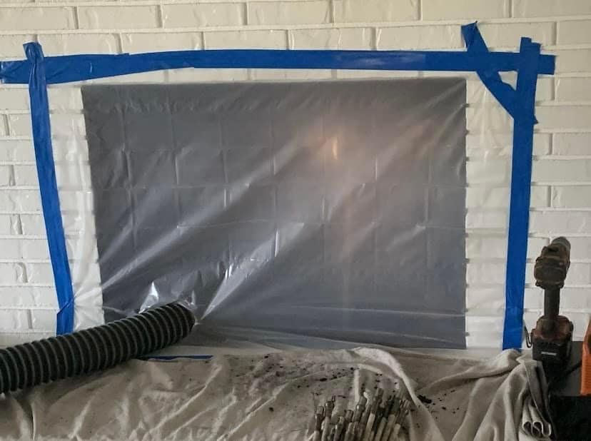 Plastic-covered window taped with blue painter’s tape in a room under renovation