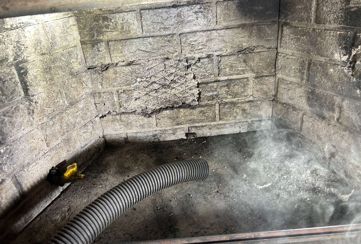 Damaged stone corner with a black corrugated hose and steam or smoke rising from the floor