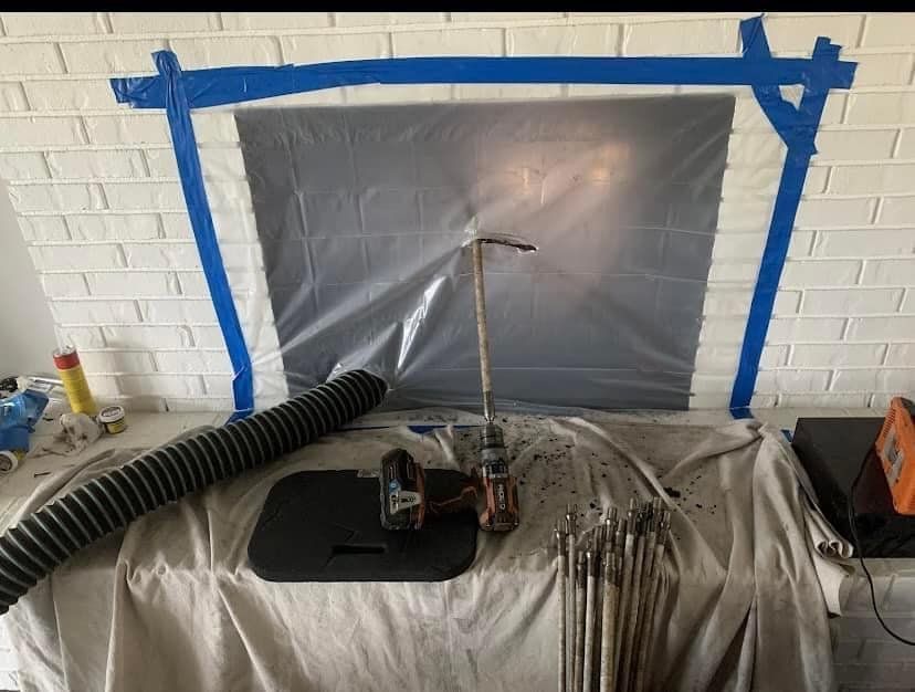 Workshop table covered with tarp, spray setup, and blue-taped plastic sheeting on a brick wall
