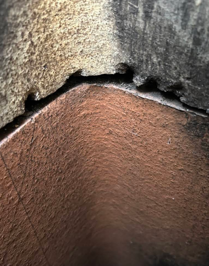 Close-up of a rough stone corner with a reddish-brown wall and dark crevice above it