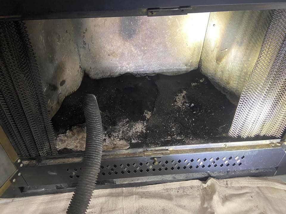 Sooty fireplace firebox with charred debris, a flexible hose in front, and white ash insulation on the back wall