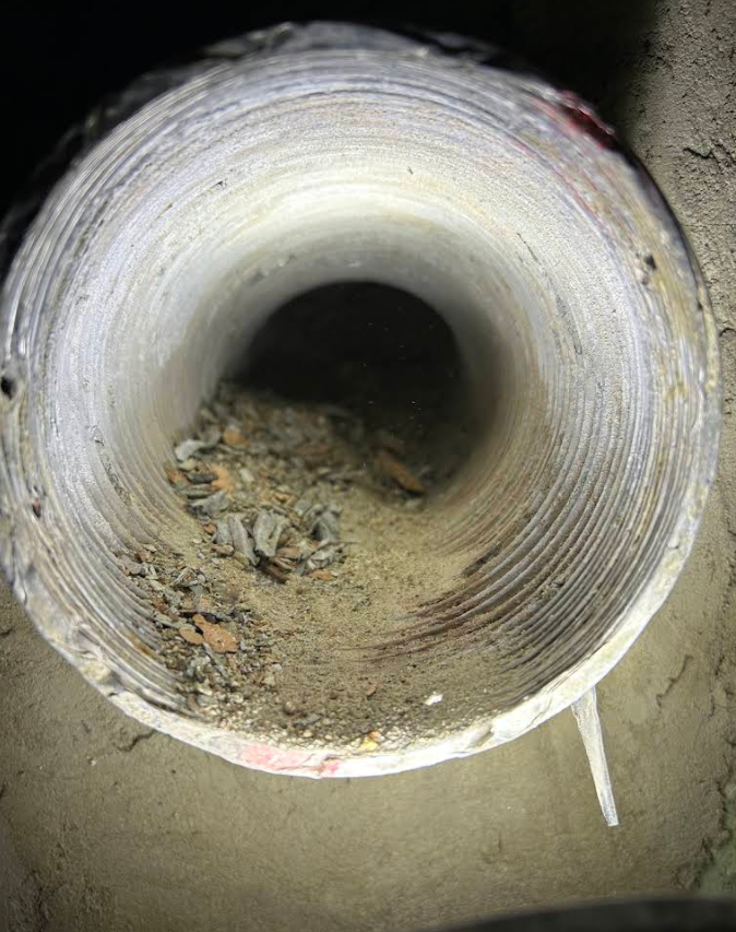 Close-up of a dirty cylindrical pipe opening with debris inside and a rough concrete surround