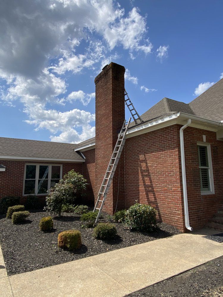 Brick house exterior with ladder leaning against a chimney under a partly cloudy sky