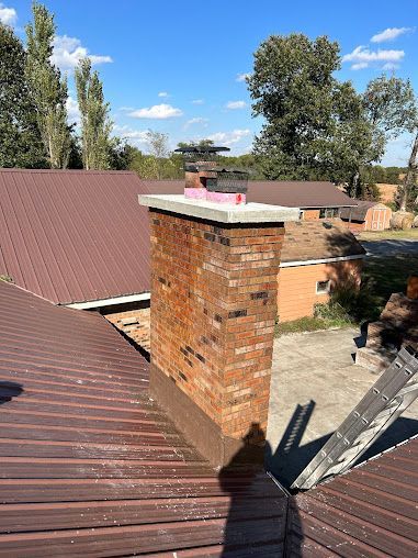 Rooftop view of brick chimney and rust-colored metal roofs under a clear blue sky.