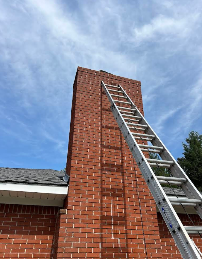 Aluminum ladder leaning against a red brick chimney on a house roof under a blue sky