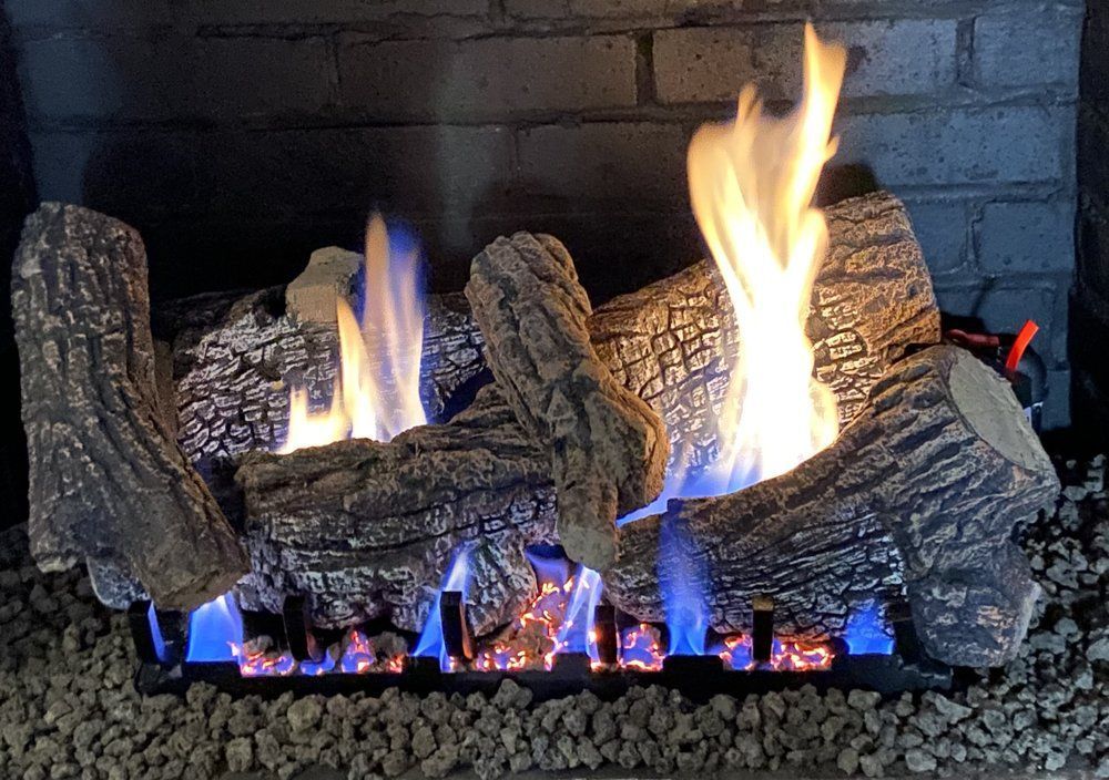 Gas fireplace with glowing logs and blue-orange flames against a dark brick backdrop