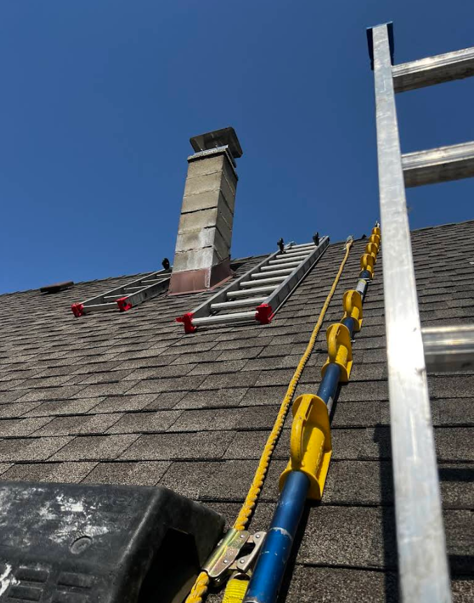 Ladder leaning on a roof beside a chimney under a clear blue sky