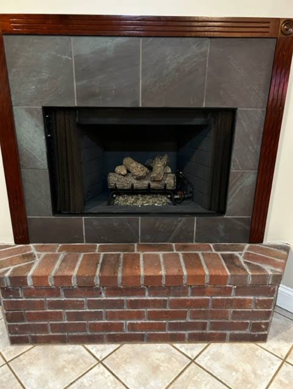 Brick fireplace with dark wood mantel, gray tile surround, and a gas firebox on a tiled floor