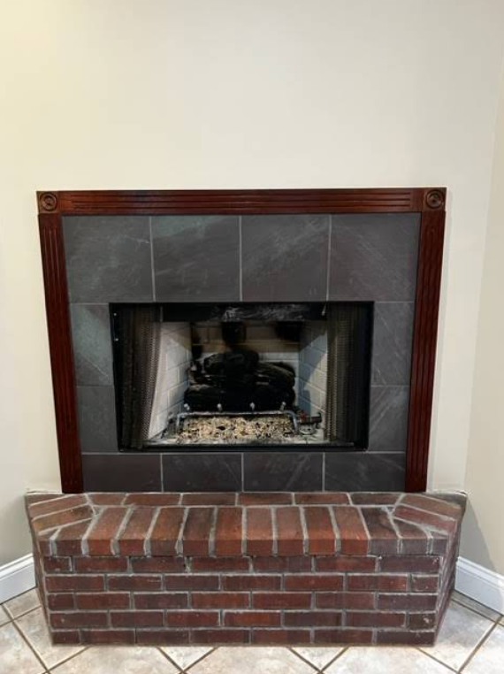 Brick fireplace with dark tile surround and red-brick hearth against a white wall