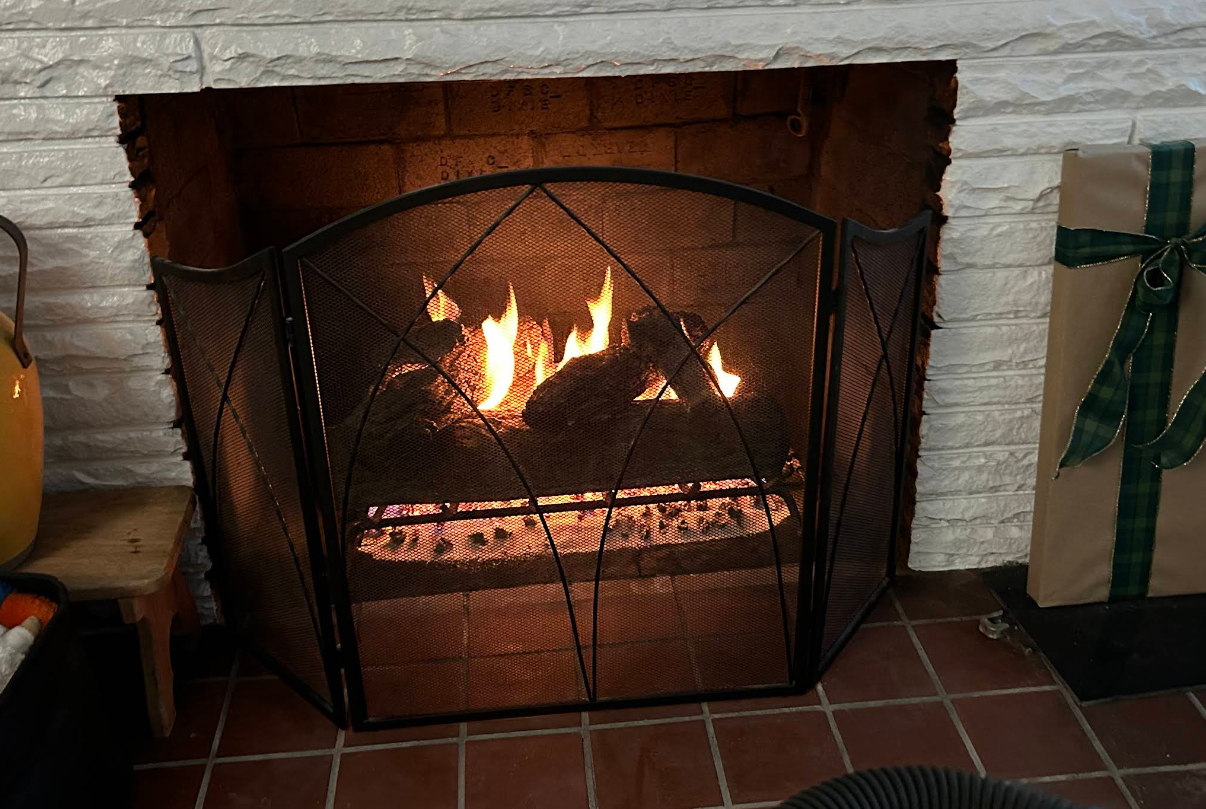 Lit fireplace with a black metal screen in a brick hearth.