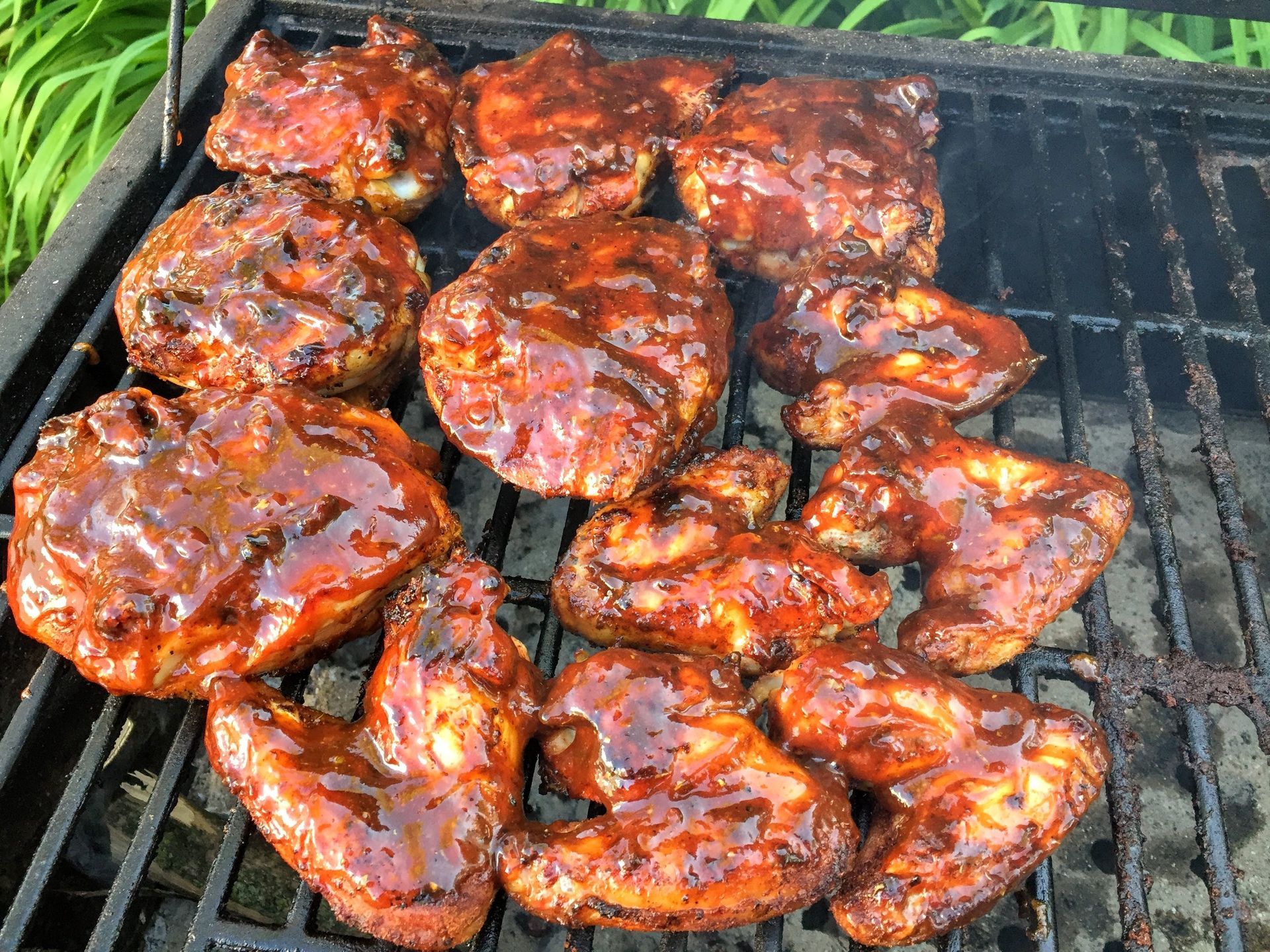 Barbecued chicken pieces on a grill, coated in a dark, glossy sauce.