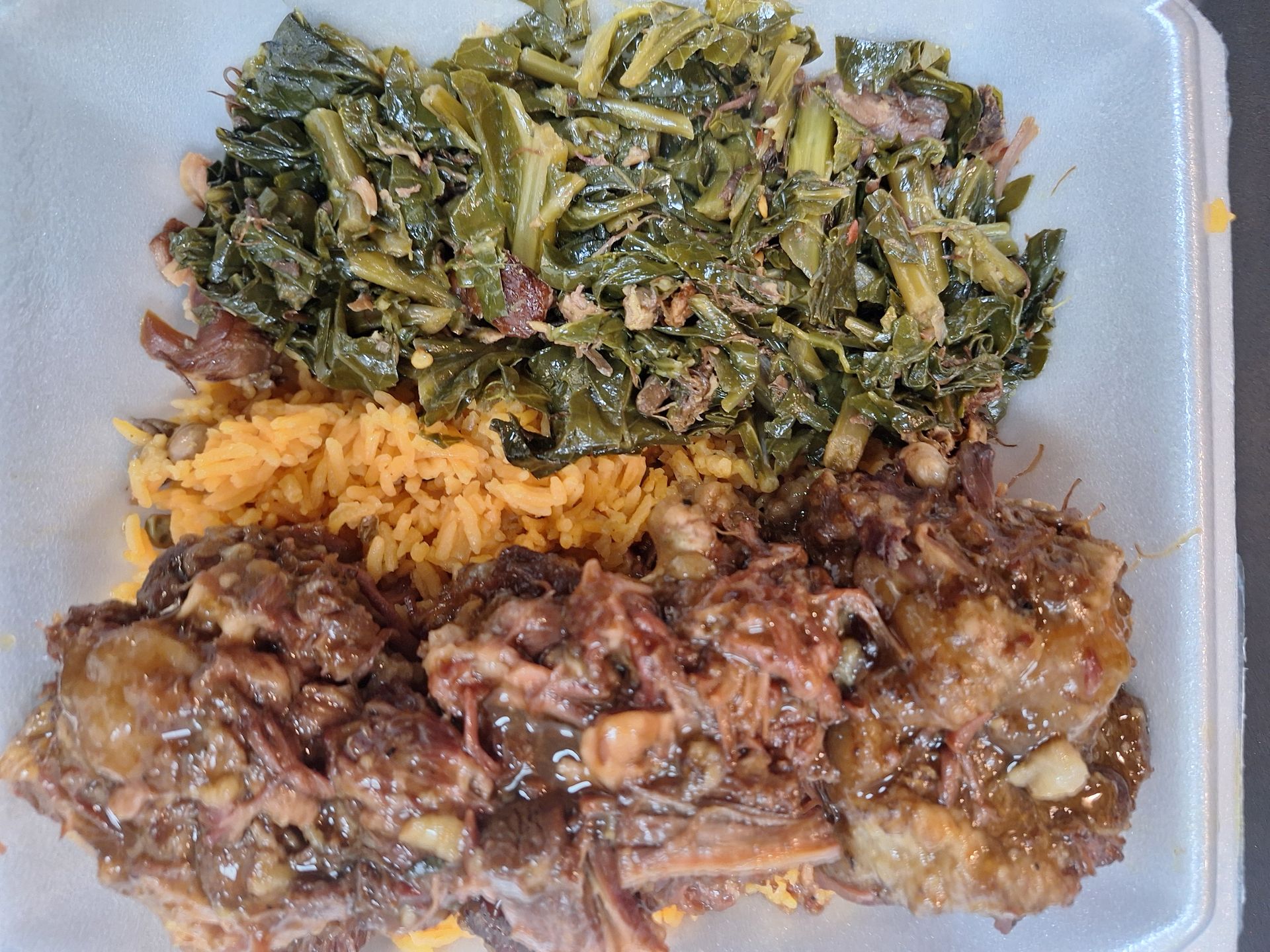 Meal in a white takeout container: collard greens, yellow rice, and braised meat with visible bones.