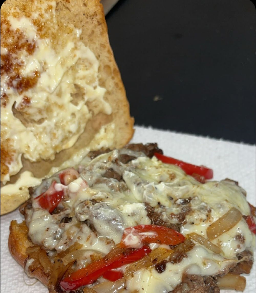 Cheesesteak sandwich with caramelized onions, red peppers, and melted cheese on toasted bread.