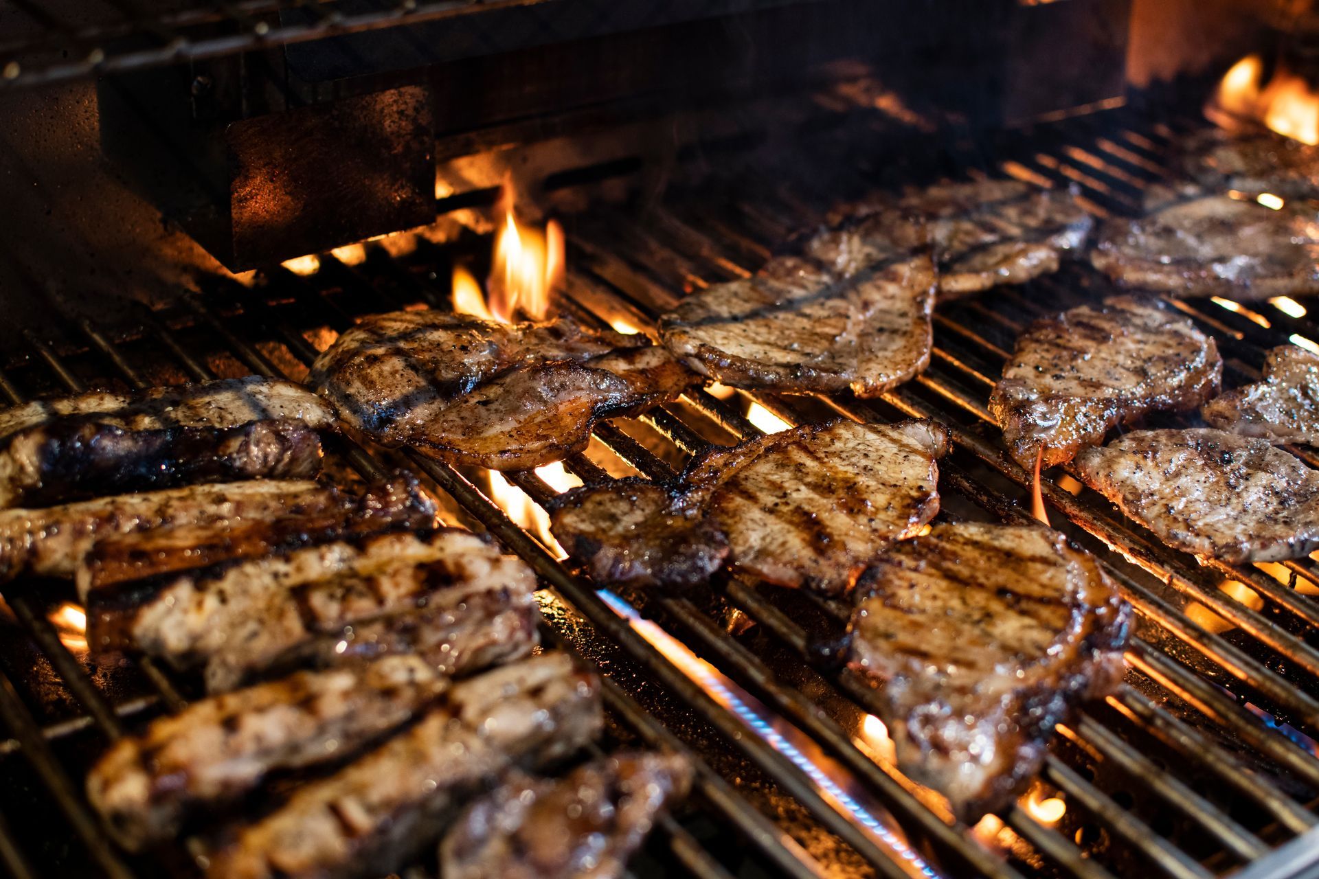 Meat grilling on a barbecue, flames visible, close-up shot of the cooking food.