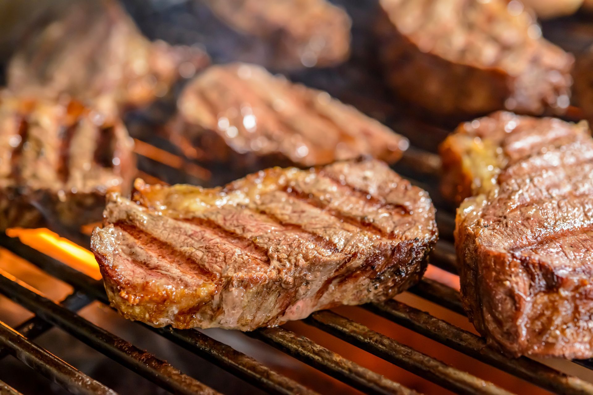 Grilled steaks on a hot barbecue grill with visible grill marks and flames.