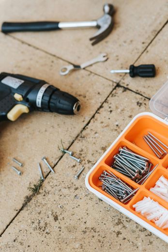 Tools and nails on a tiled floor, with an orange organizer tray and a cordless drill nearby