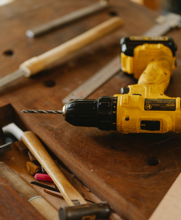 Yellow cordless drill with bit on a wooden workbench рядом with pencils and hand tools