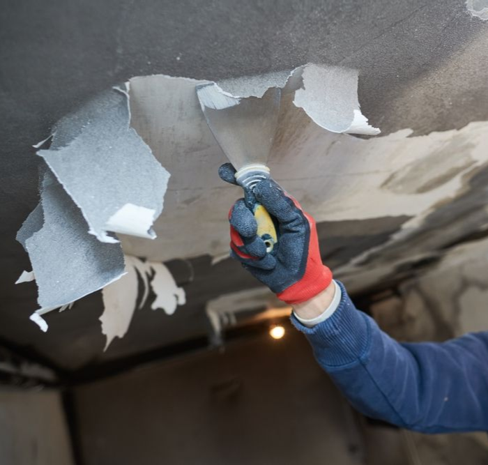 Gloved hand peeling damaged drywall from a ceiling crack