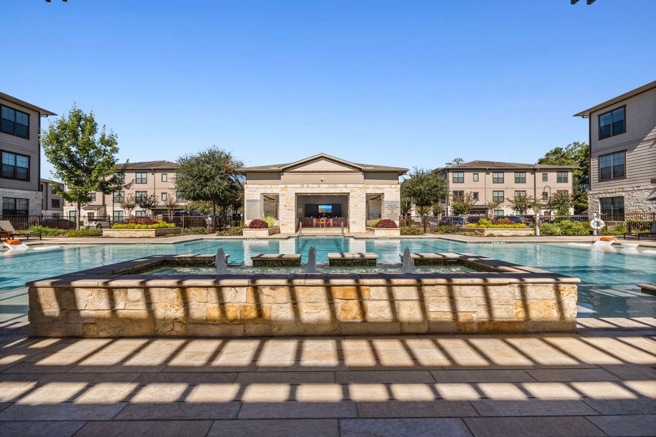 Outdoor community pool with a central stone fountain and surrounding lounge areas.