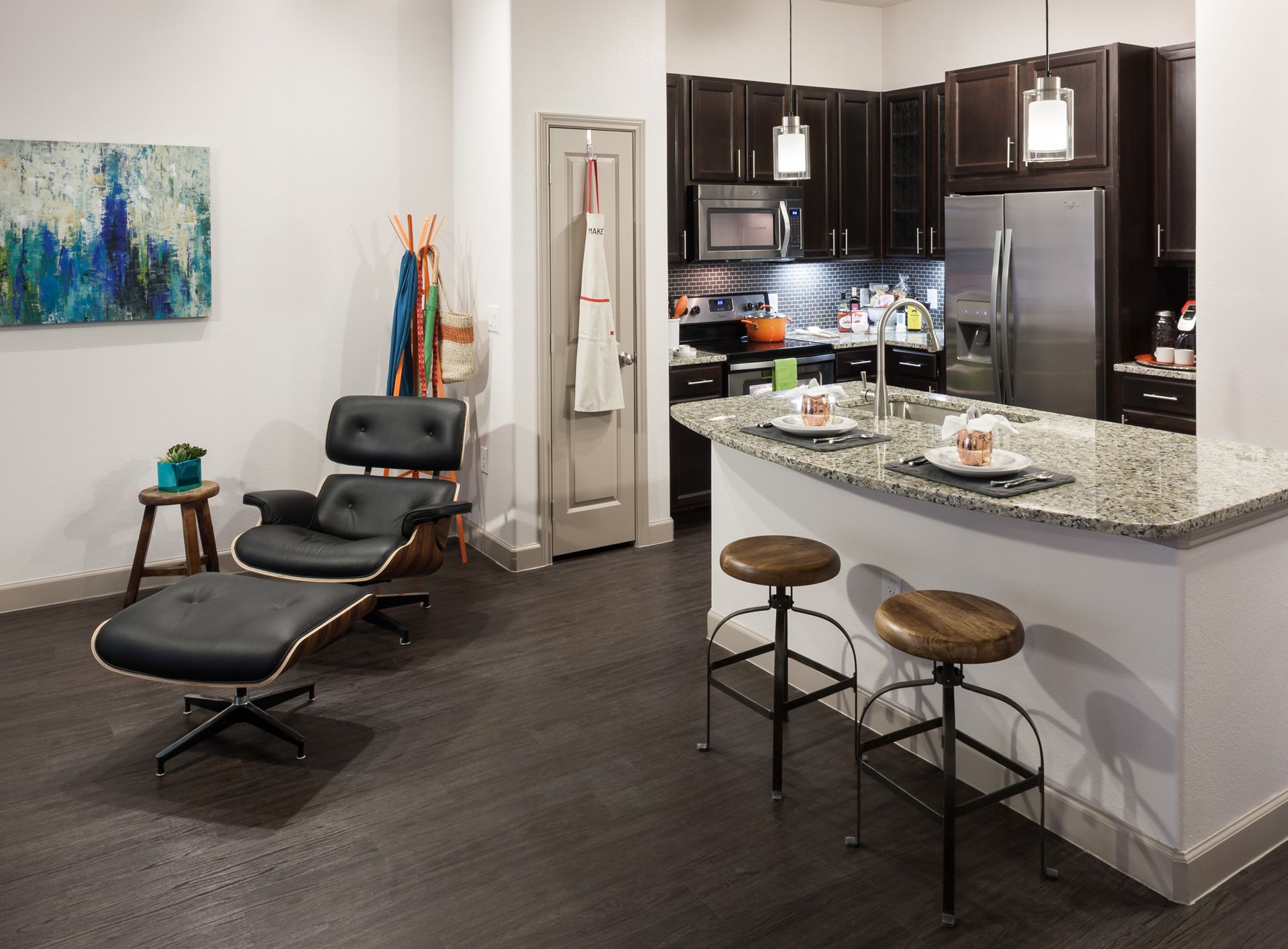 Open-concept living area with kitchen island, bar stools, dark wood floors, and stainless appliances.