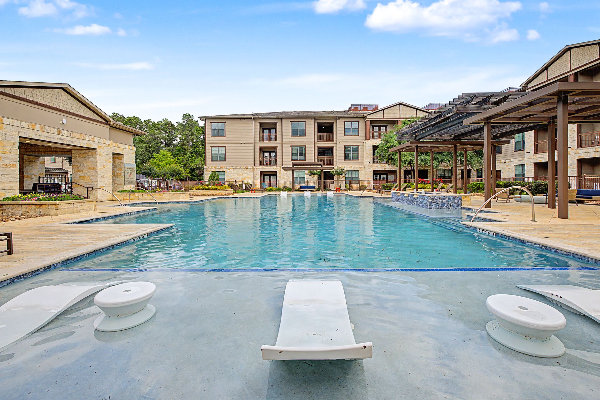 Resort-style outdoor pool with lounge chairs and cabanas under a bright blue sky at Olympus Auburn Lakes in Spring, TX.